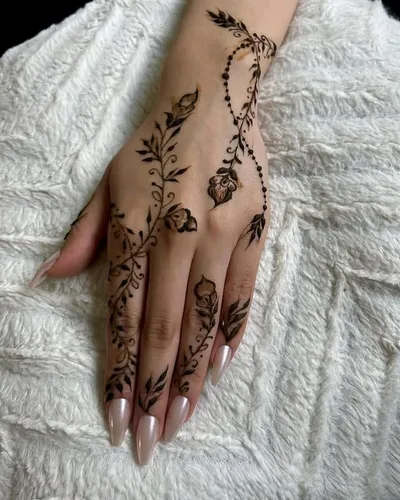 A floral henna design trailing up the hand and fingers, with long nude stiletto nails